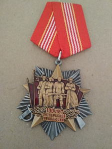 Знак на пятиугольной колодке "100 лет Октябрьской революции". На фоне пятиконечной звезды четыре революционера.